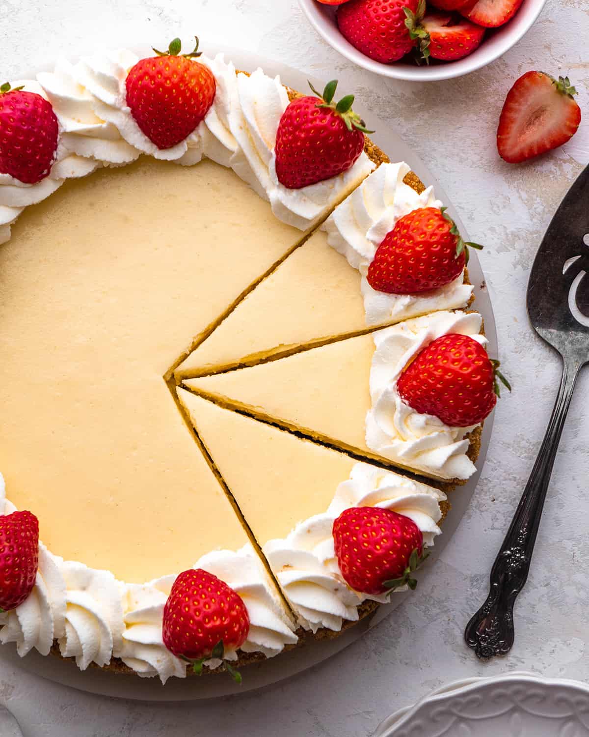 a cheesecake decorated with whipped cream and strawberries with 3 slices cut out of it