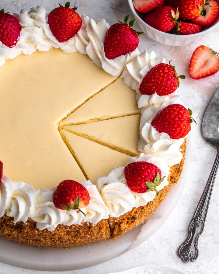 a classic cheesecake decorated with whipped cream and strawberries with three slices cut out of it