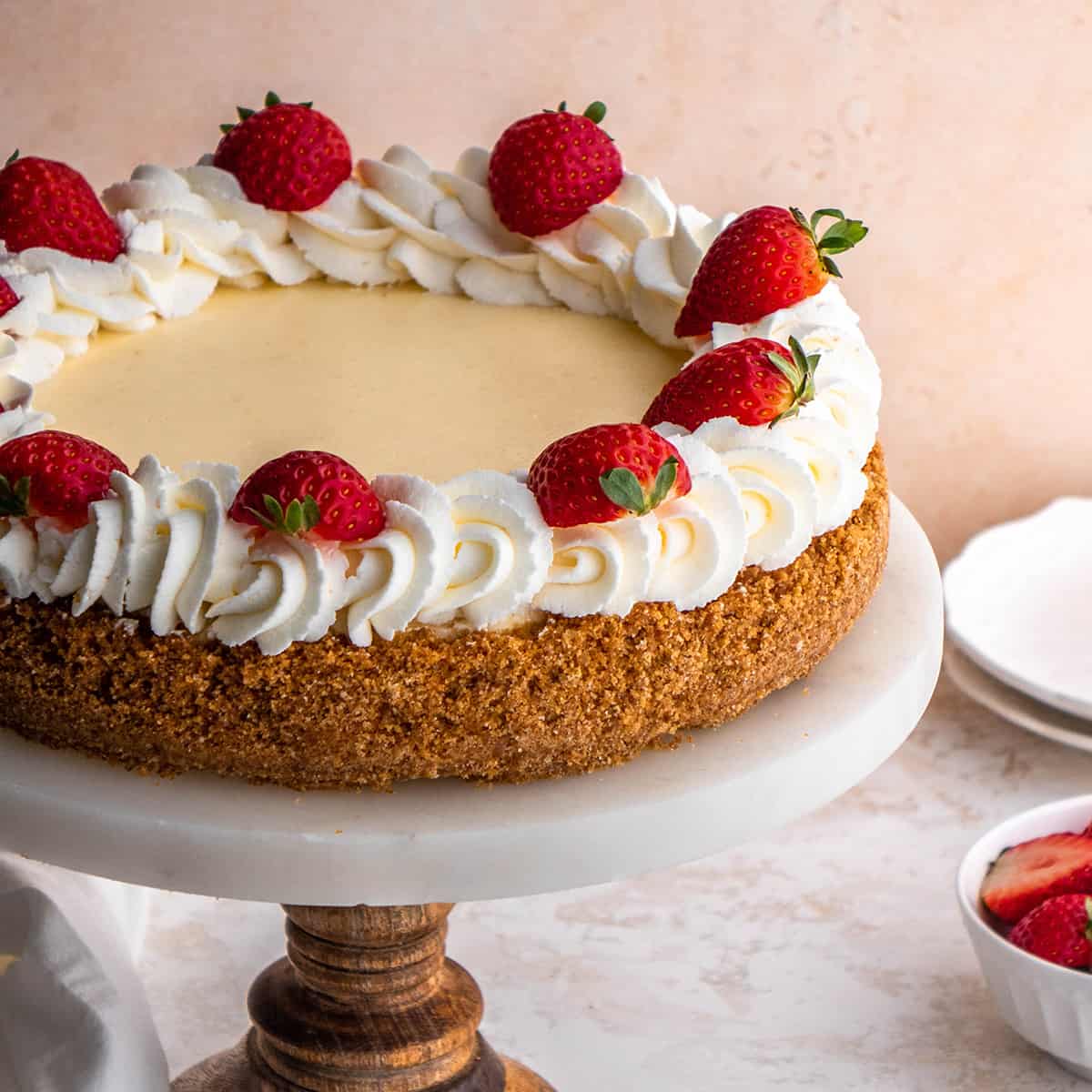 a classic cheesecake decorated with whipped cream and strawberries on a cake plate