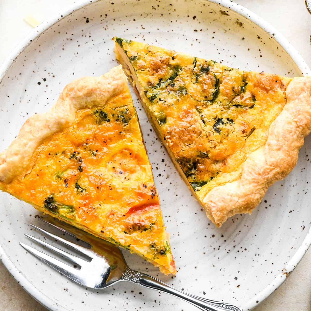 two slices of quiche on a plate - one vegetable quiche one spinach bacon quiche