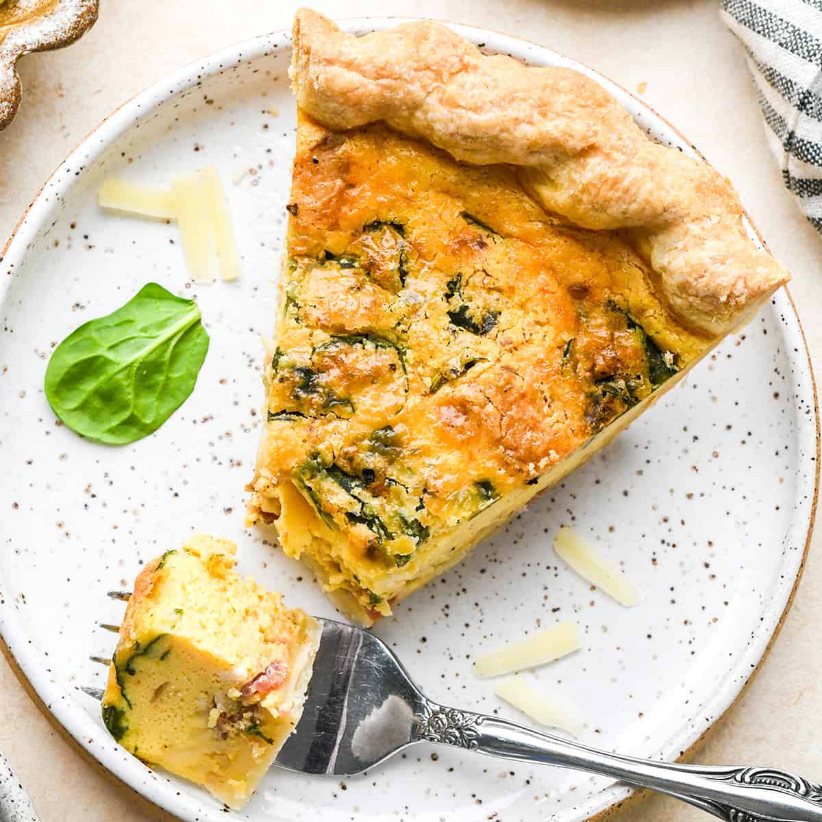 a piece of Best Easy Quiche on a plate with a fork that has a bite on it
