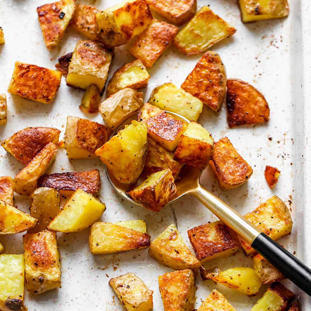 a spoon scooping Oven Roasted Potatoes off of a baking sheet