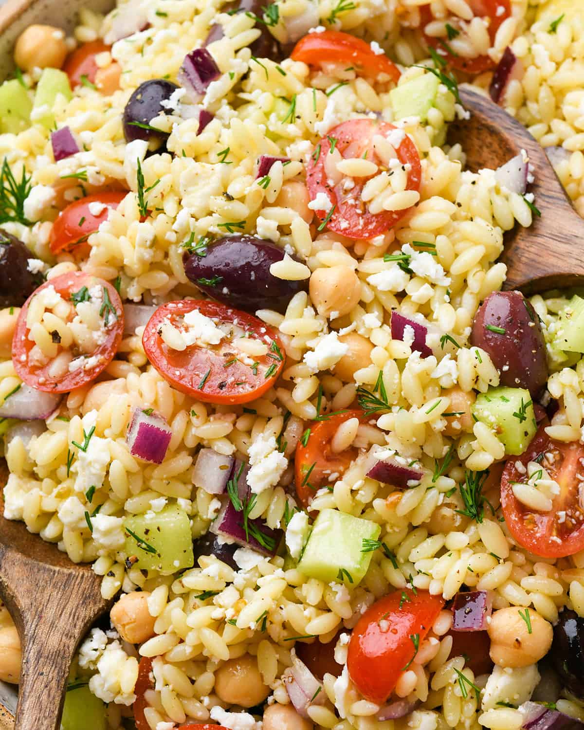 up close photo of Greek Orzo Salad with a serving spoon taking a scoop
