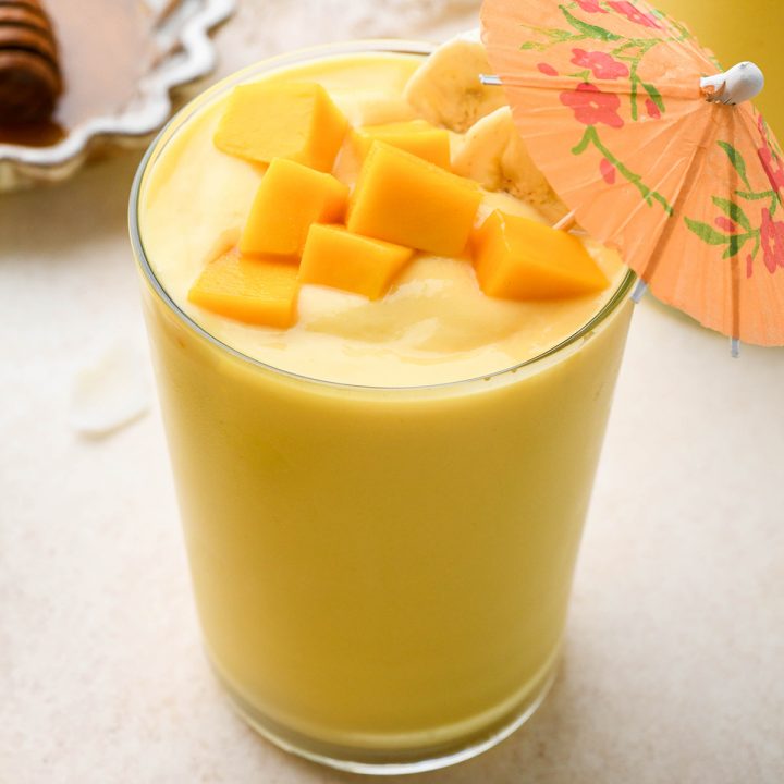 tropical smoothie in a glass topped with mango and banana and a drink umbrella