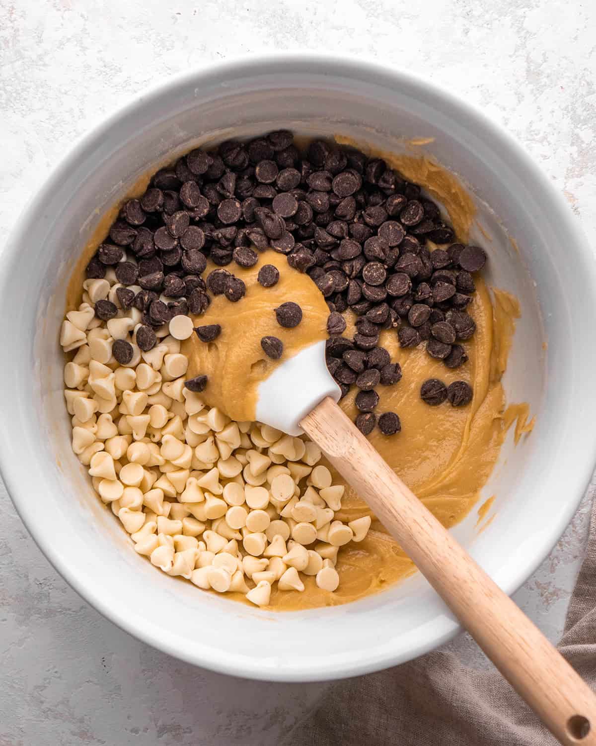 how to make blondies - white chocolate chips and semisweet chocolate chips added to the blondies recipe batter in a white bowl with a spatula before being mixed in
