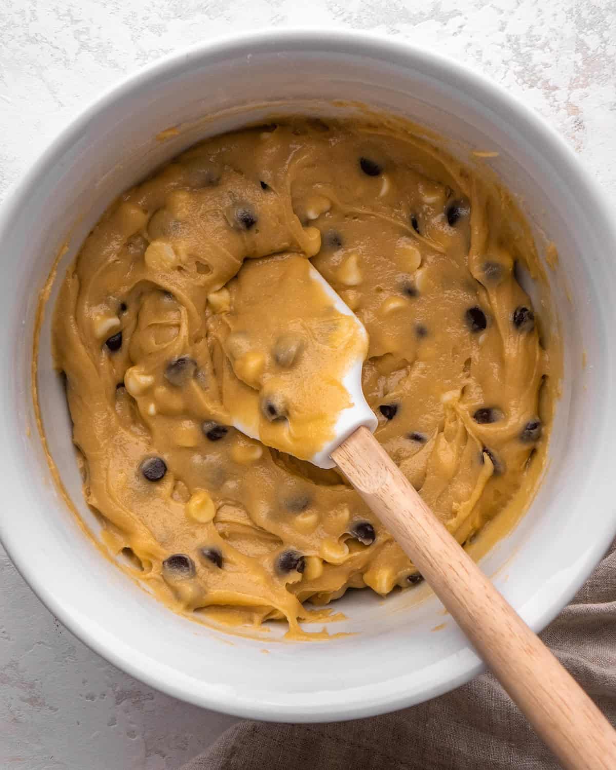 blondies recipe batter in a white bowl after the baking chips have been mixed in with a white silicone spatula with a wood handle.