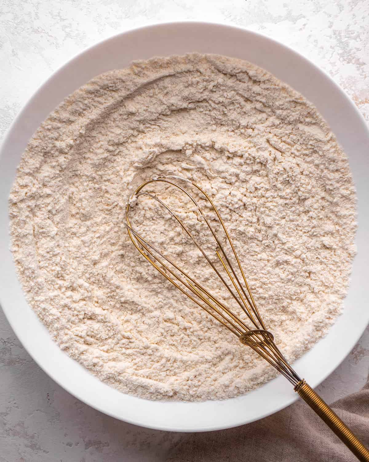 how to make blondies - flour mixture in a white bowl after being mixed together with a gold whisk that is in the bowl