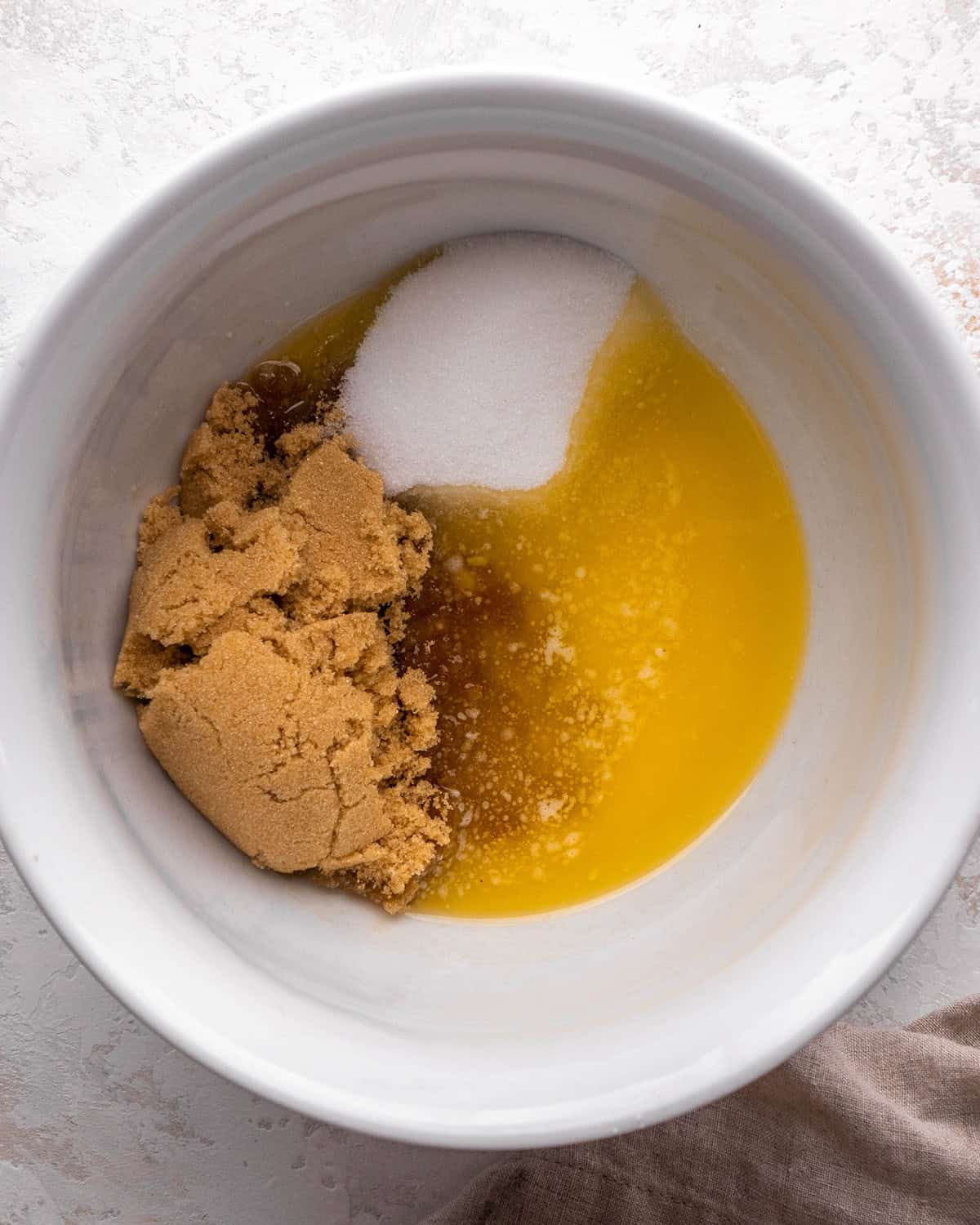 how to make blondies - melted butter, white sugar and light brown sugar in a white bowl on a gray surface before mixing