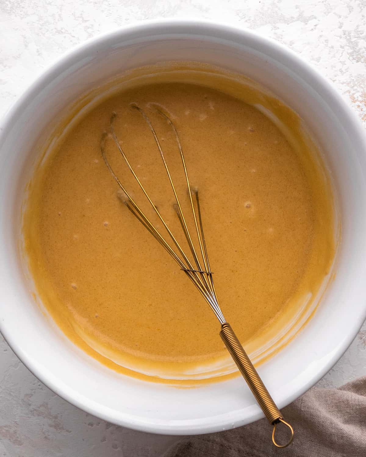how to make blondies - wet ingredient mixture in a white bowl after mixing, there is a gold whisk int eh bowl.
