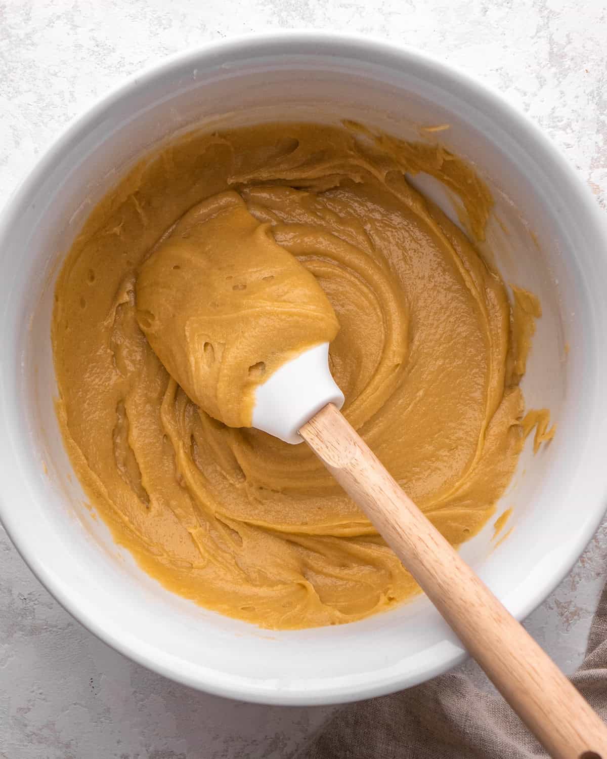 how to make blondies - blondies batter in a white bowl with a white silicone spatula with a wood handle