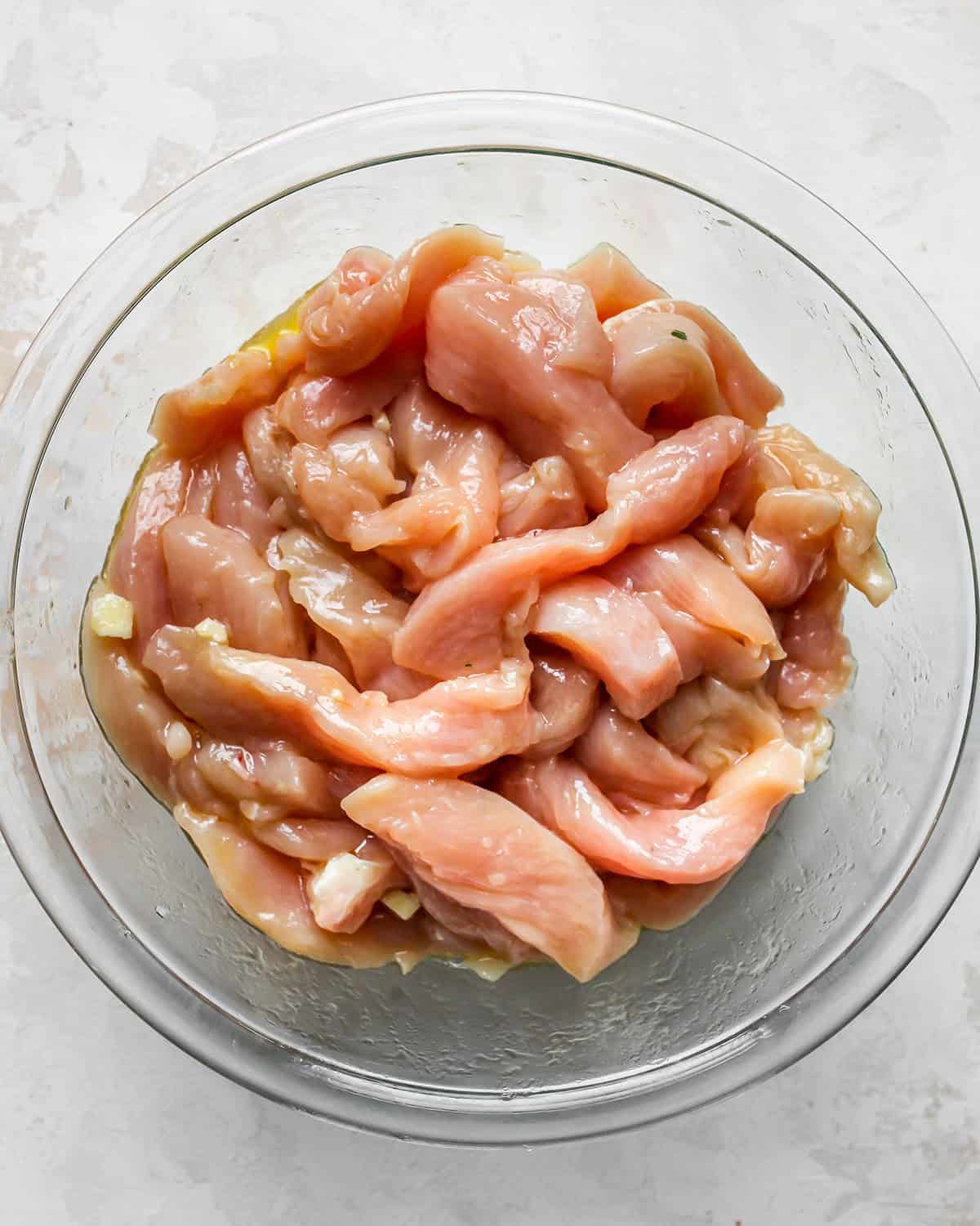 how to make chicken fajitas - chicken sliced into thin strips coated with chicken fajitas marinade in a glass bowl
