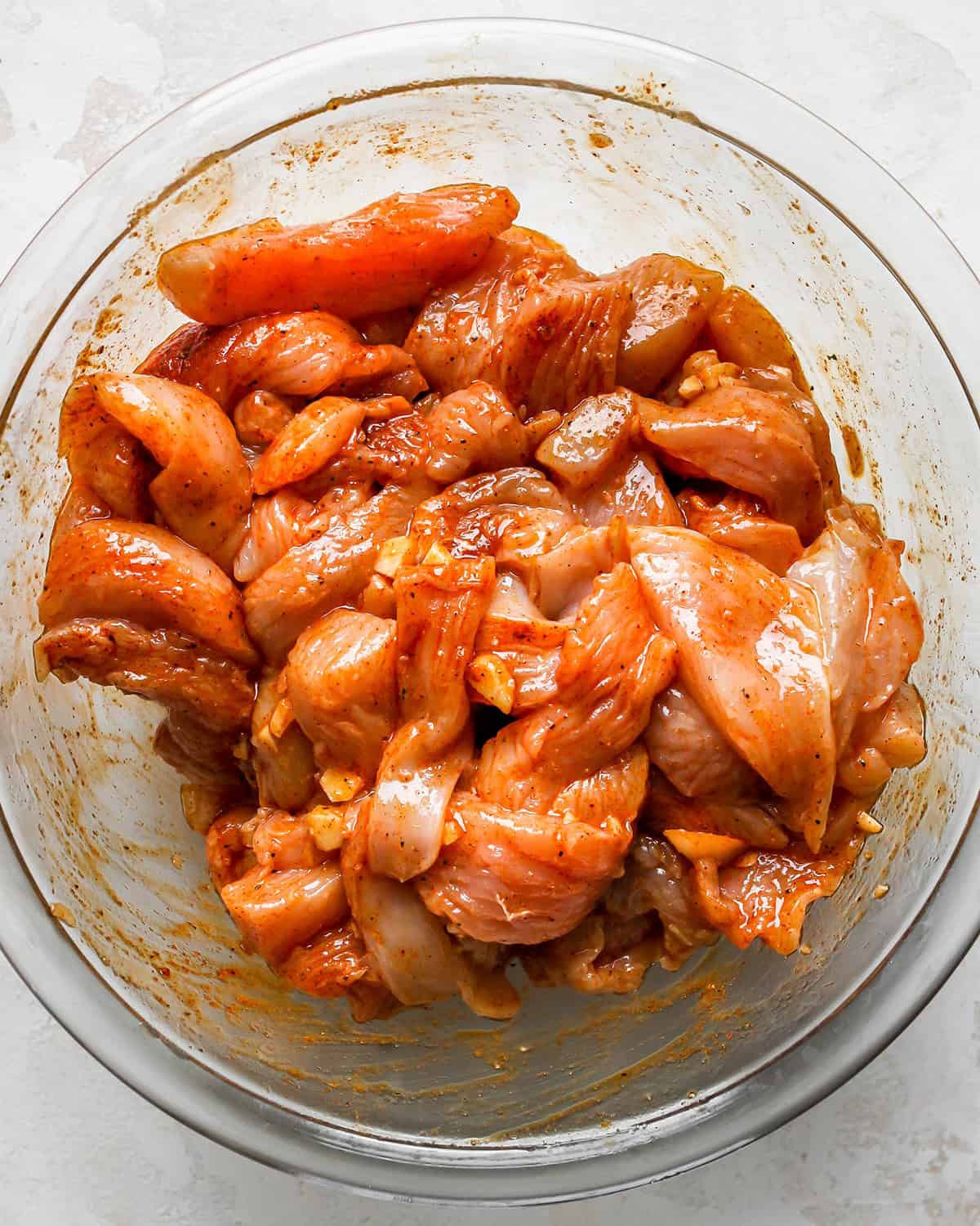 how to make chicken fajitas - chicken sliced into thin strips coated with chicken fajitas seasoning in a glass bowl