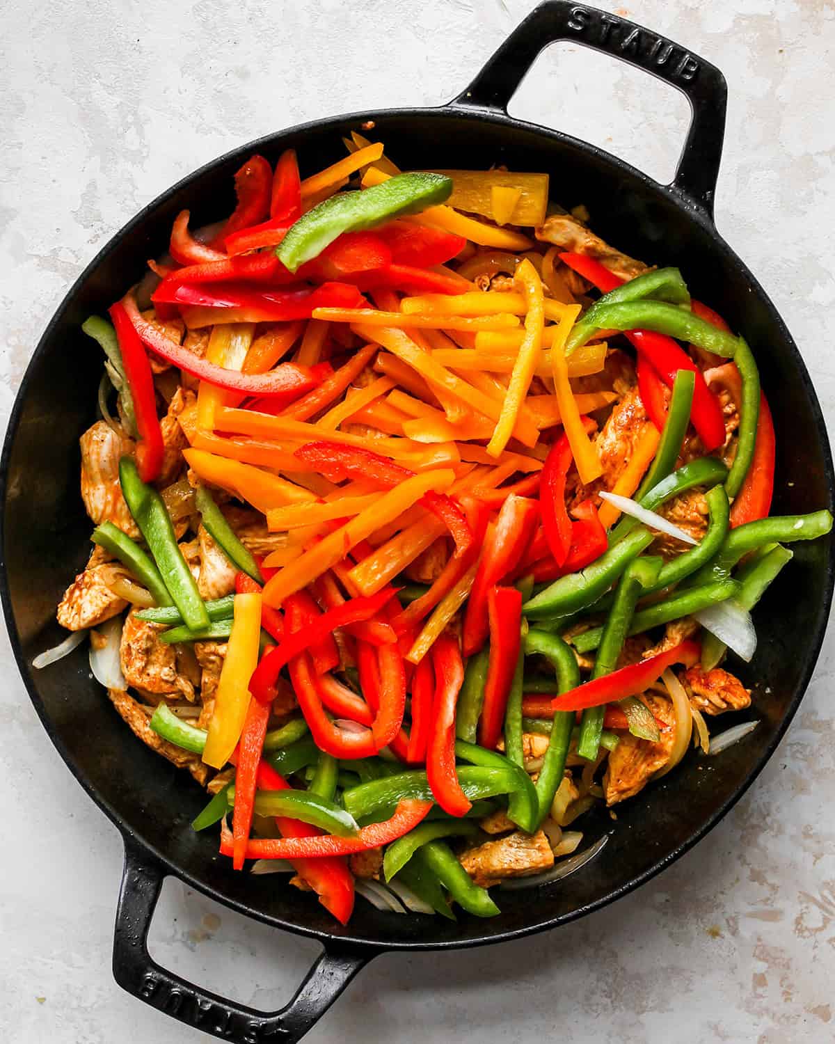 making chicken fajitas - red, orange and green bell peppers added to the cooked chicken and onions in a black cast iron skillet before the peppers are cooked