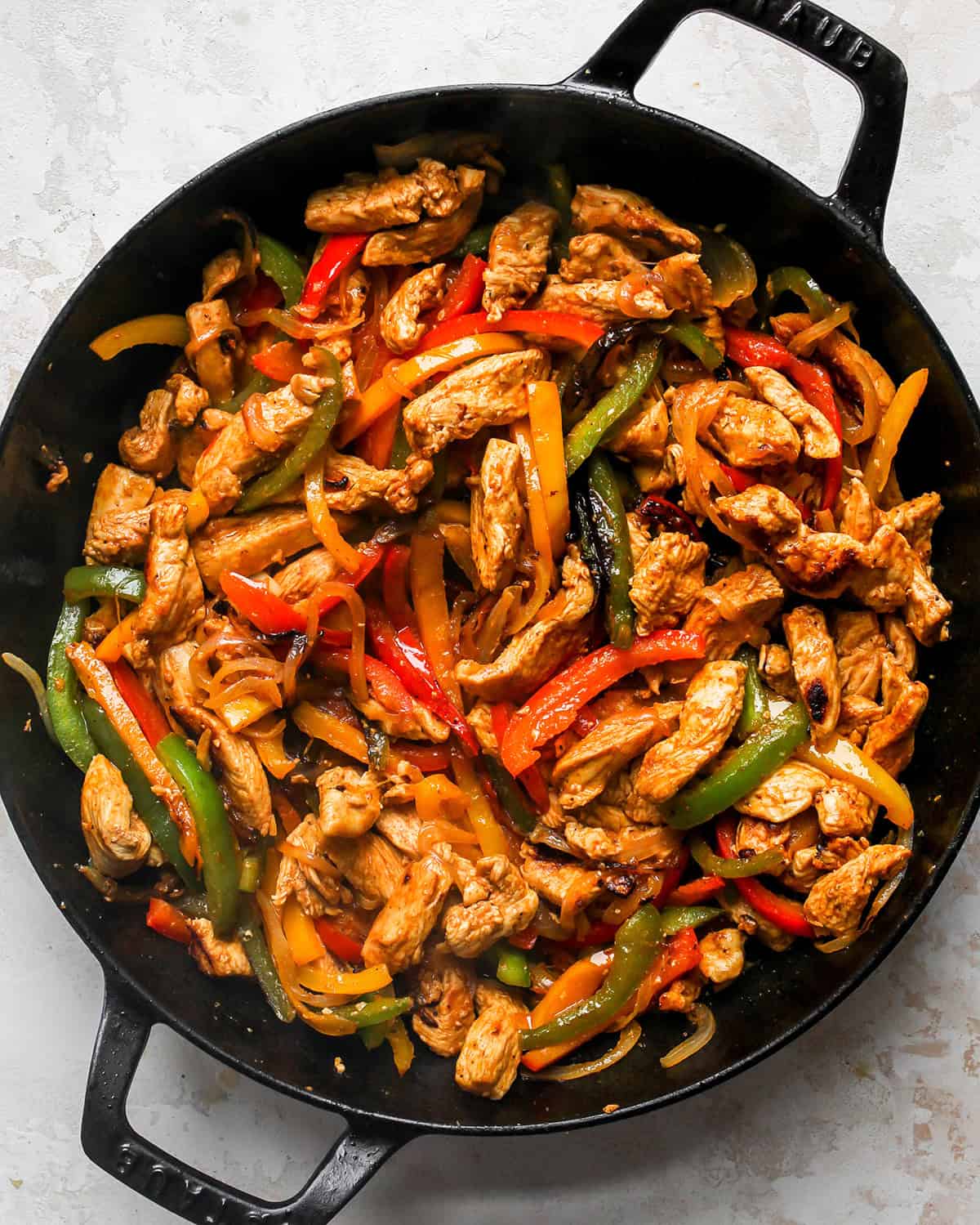 cooked chicken fajitas with red, orange and green bell peppers in a black cast iron skillet