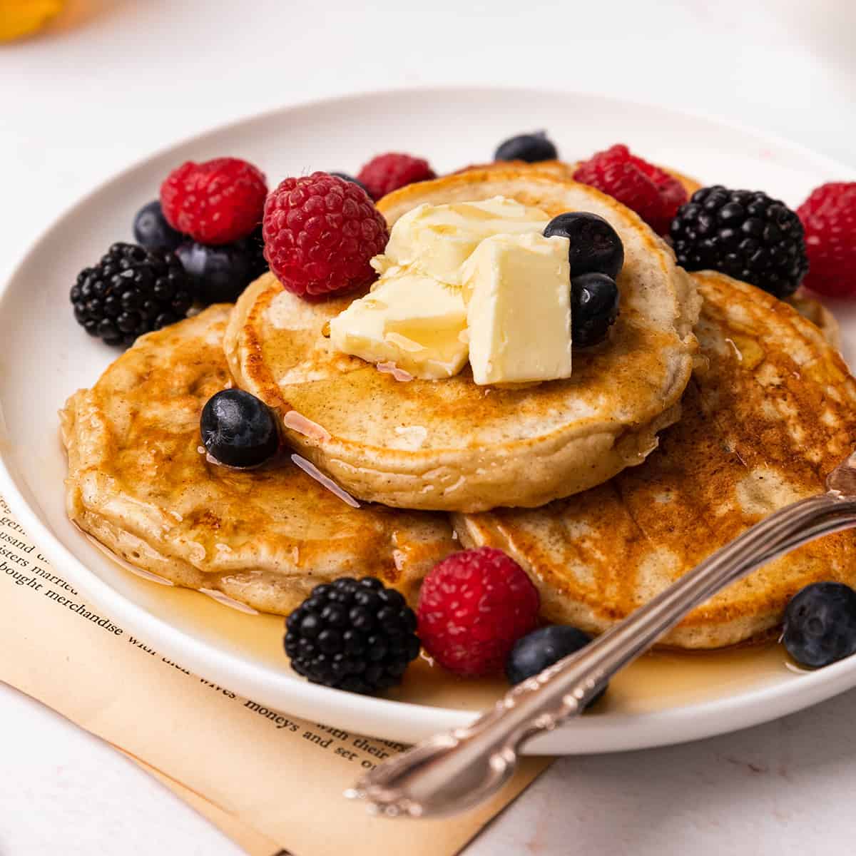 4 Cottage Cheese Pancakes on a plate with butter, syrup and berries