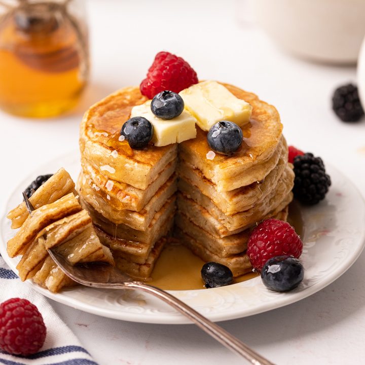 a stack of 6 Cottage Cheese Pancakes with a bite taken out of it on a fork with butter, syrup and berries
