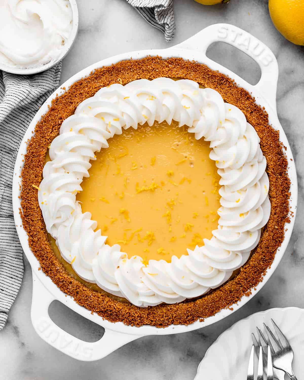 a Lemon Pie Recipe in a white pie dish topped with whipped cream and lemon zest