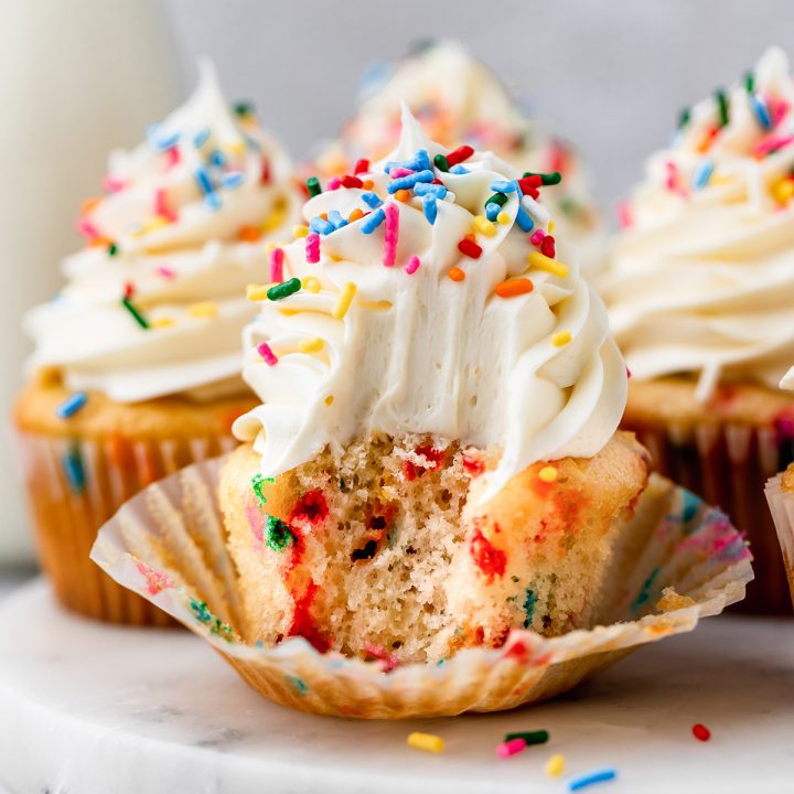 Funfetti Cupcake with vanilla frosting and sprinkles & a bite taken out of it