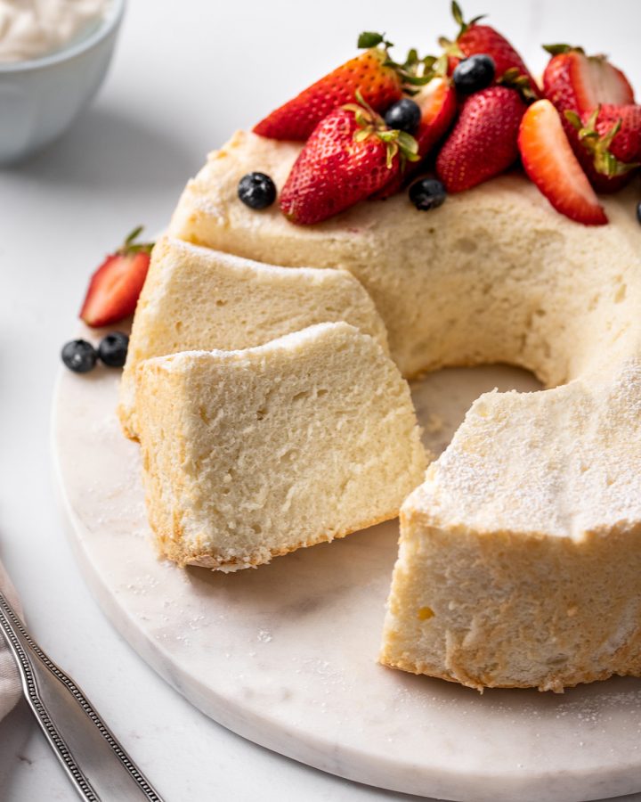Homemade Angel Food Cake with two slices cut out of it and berries on top