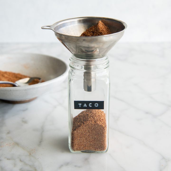 photo showing How to Make Taco Seasoning - pouring the seasoning into a glass spice jar with a funnel.