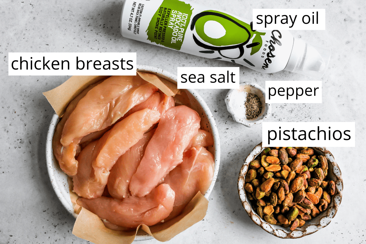 overhead photo of the labeled ingredients in this pistachio chicken recipe like sea salt, chicken breasts, oil, pistachios and pepper