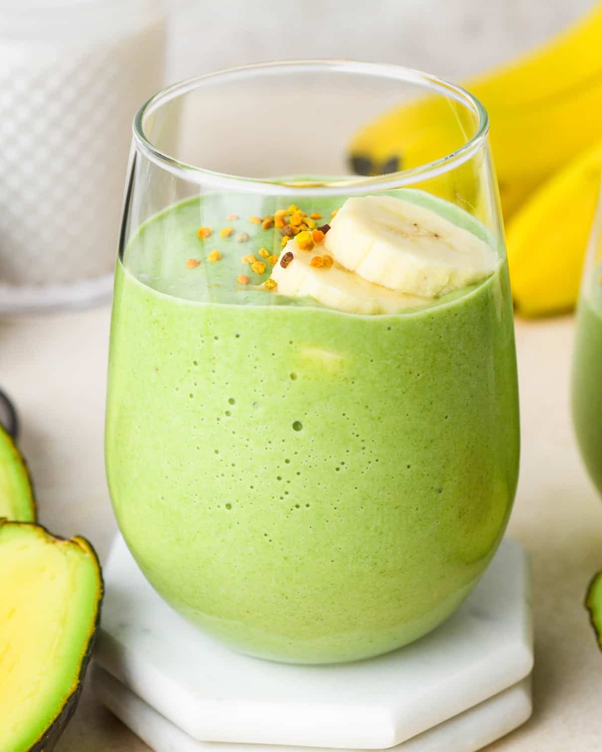 a glass of avocado smoothie topped with sliced bananas and bee pollen