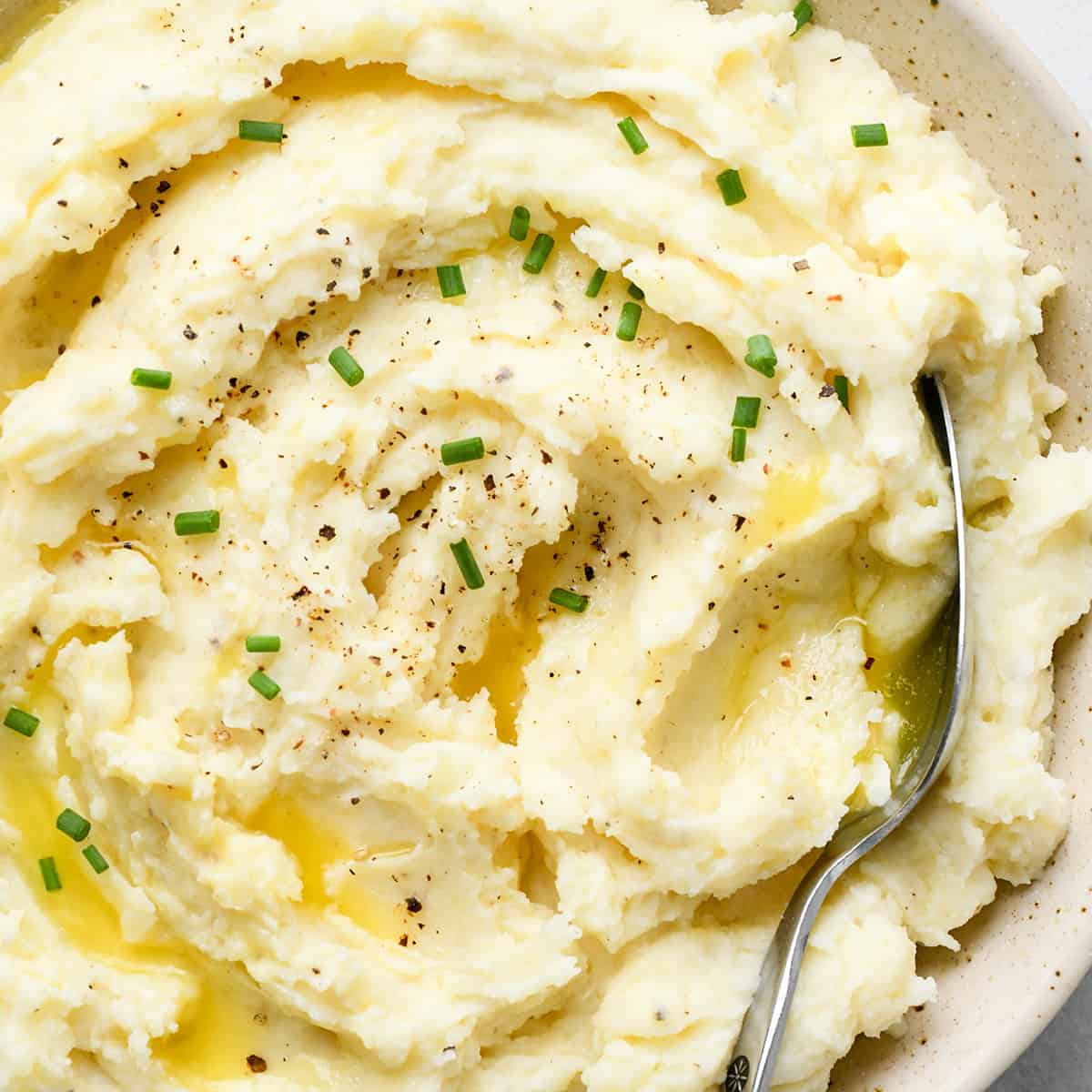 Cream Cheese Mashed Potatoes in a bowl with butter, chives, and a spoon 