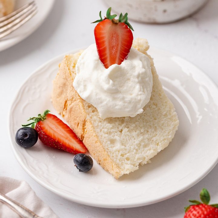 a slice of Angel Food Cake on a plate with whipped cream and berries 