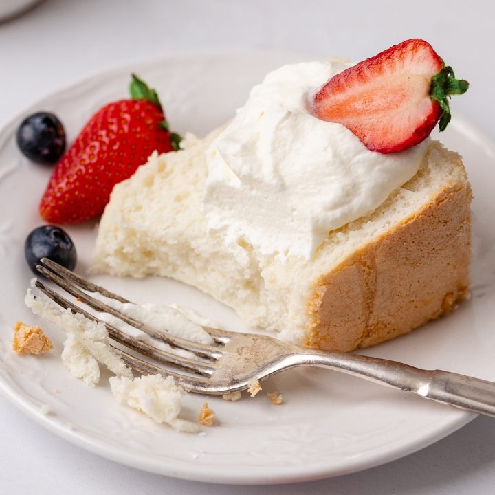 a slice of Angel Food Cake on a plate with a bite taken out of it, fork, whipped cream and berries