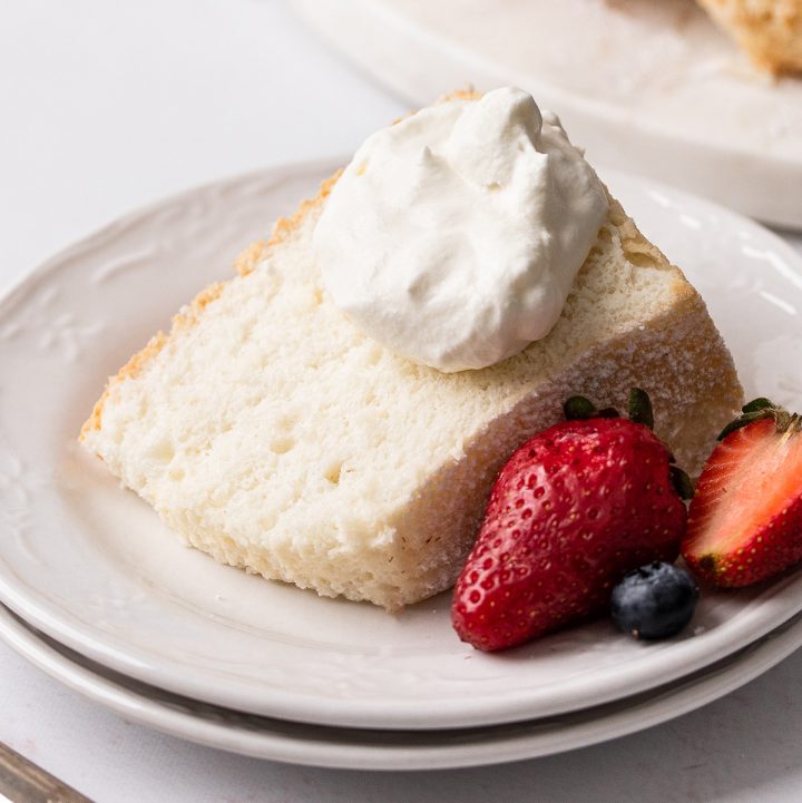 a slice of Homemade Angel Food Cake on a plate with whipped cream and berries 