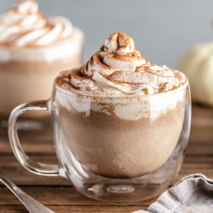 a Pumpkin Spice Latte in a glass mug with whipped cream and cinnamon