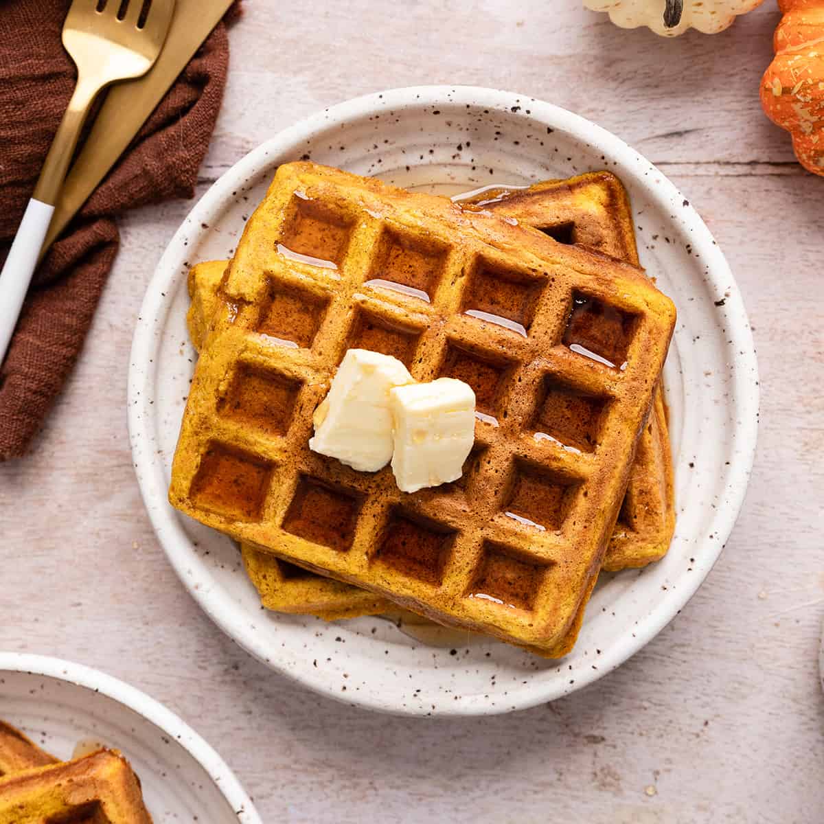 two Pumpkin Waffles on a plate with butter and syrup