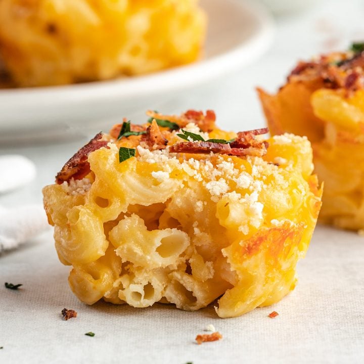 baked mac and cheese cup topped with bacon and parsley with a bite taken out of it