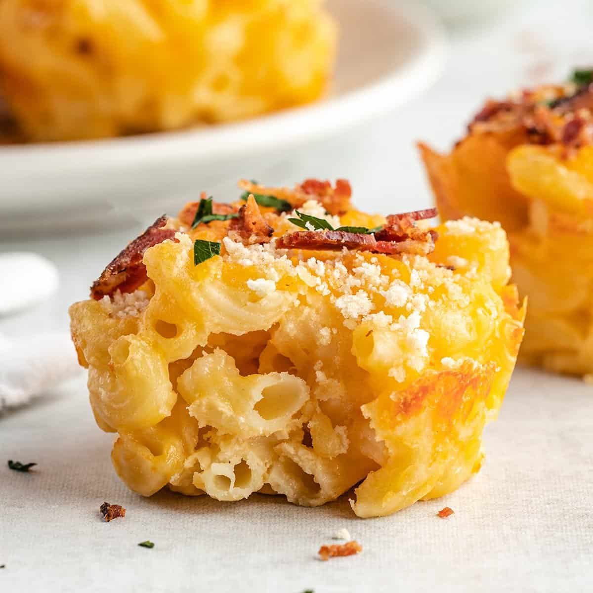 baked mac and cheese cup topped with bacon and parsley with a bite taken out of it