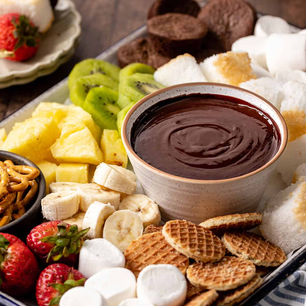 a bowl of Chocolate Fondue surrounded by chocolate fondue dippers like cookies, fruit and cake. 