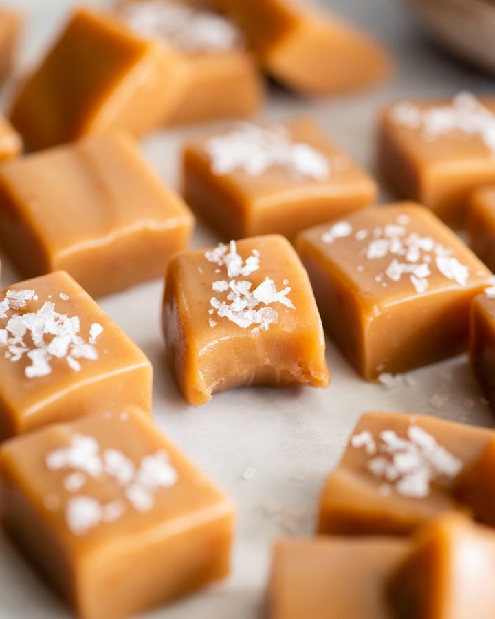 Homemade Caramel Recipe cut into squares with flaky sea salt on top, one has a bite taken out of it 
