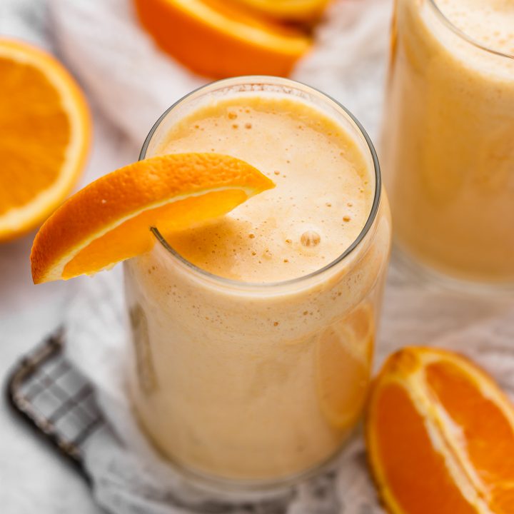 a glass of Banana Orange Smoothie garnished with an orange slice 