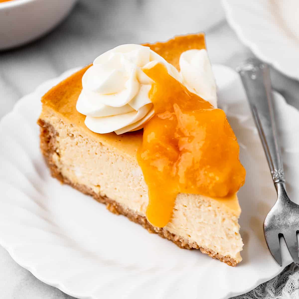 a slice of Peach Cheesecake topped with peach topping and whipped cream