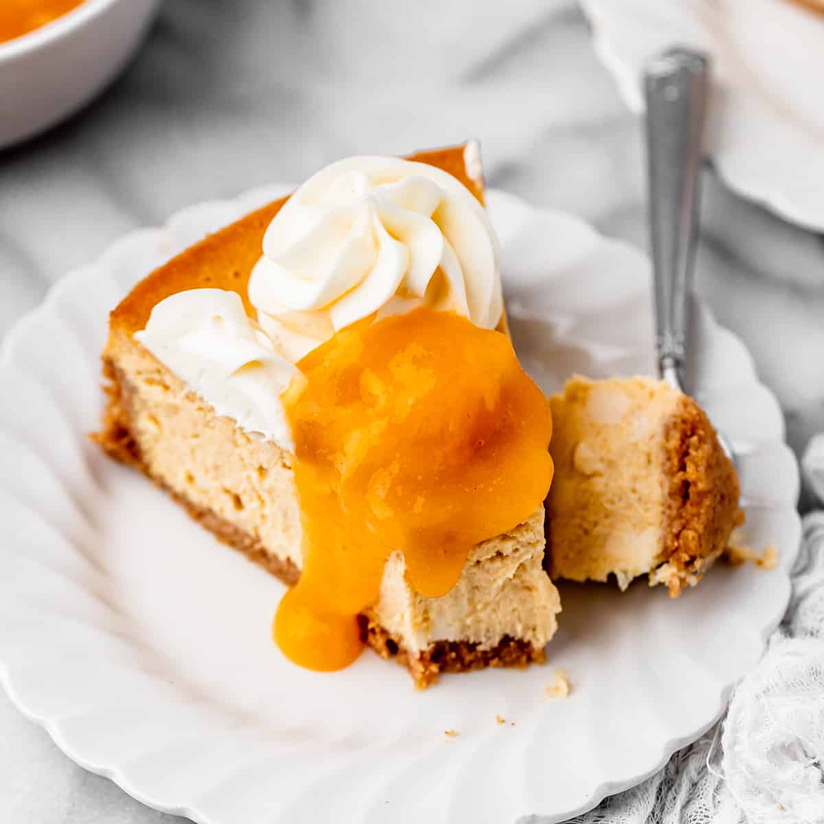 a slice of Peach Cheesecake topped with peach topping and whipped cream and a bite taken out of it