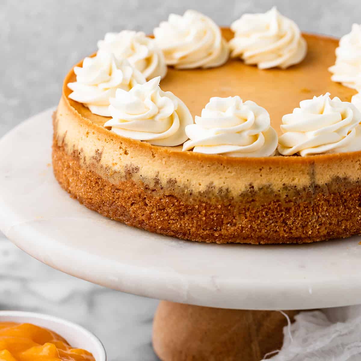 a Peach Cheesecake decorated with whipped cream on a cake stand. 