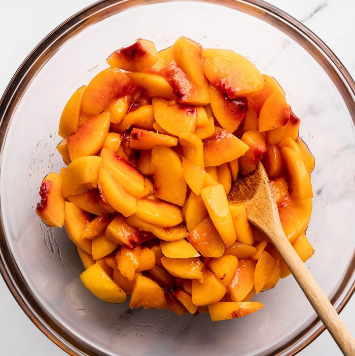 peeled sliced peaches in a bowl with a wooden spoon