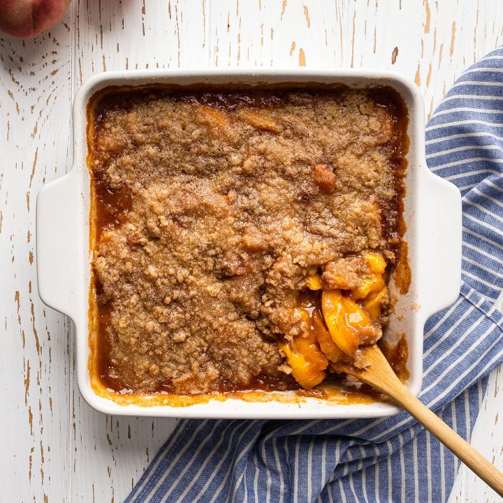 baked Peach Crumble in a baking dish with a spoon taking a scoop.