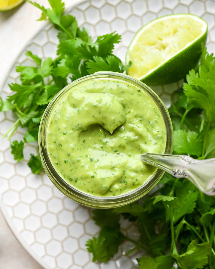 overhead view of Cilantro Lime Avocado Dressing in a glass jar with a spoon inside