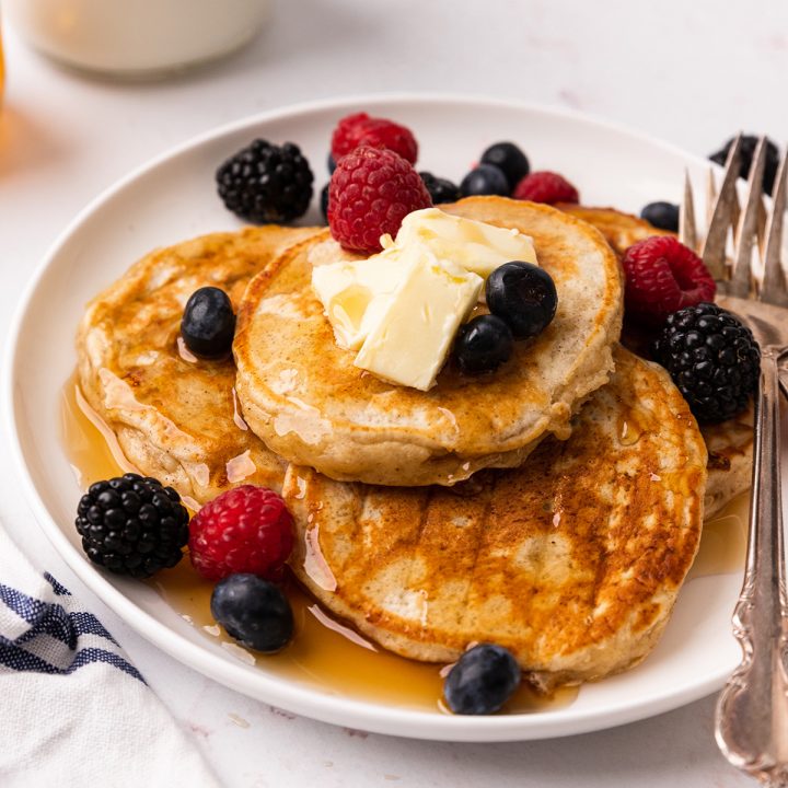 5 Cottage Cheese Pancakes on a plate with butter, berries & syrup