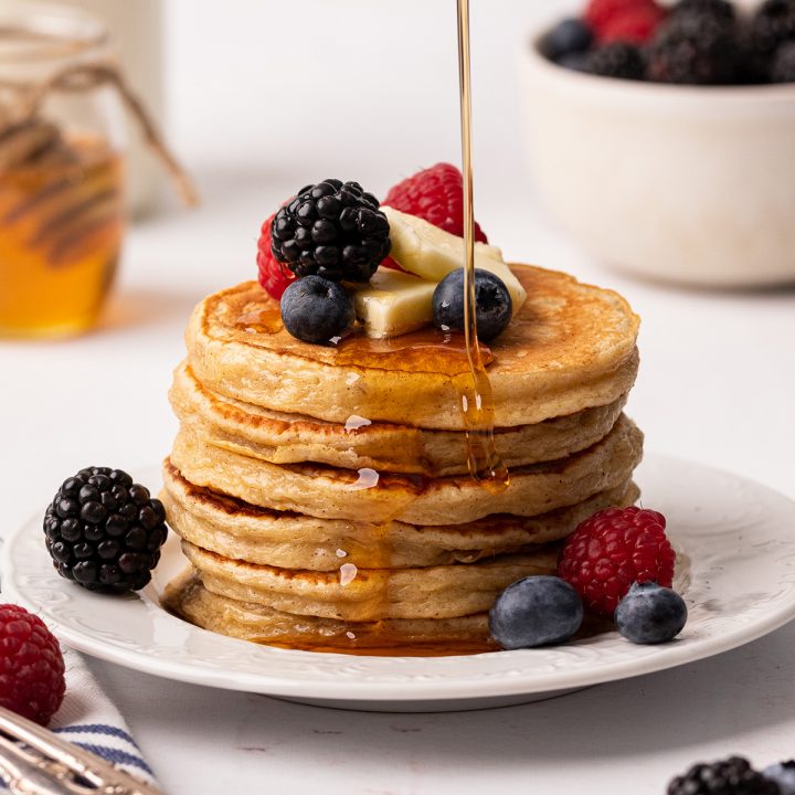 a stack of 6 Cottage Cheese Pancakes with butter, berries and syrup pouring over the top