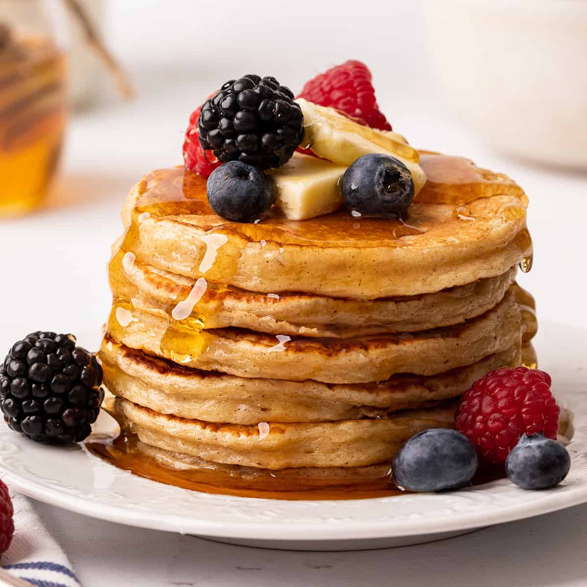 a stack of 6 Cottage Cheese Pancakes with syrup, butter and berries. 