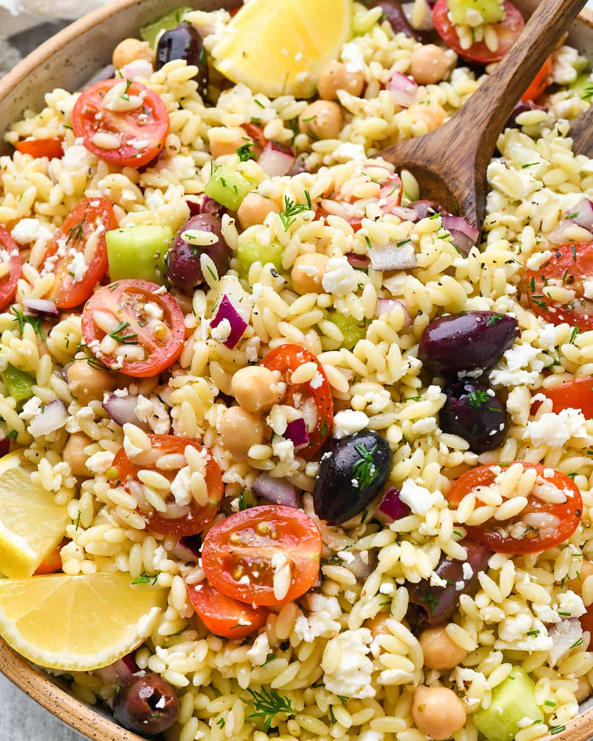 a wooden spoon taking a scoop of Mediterranean orzo salad 