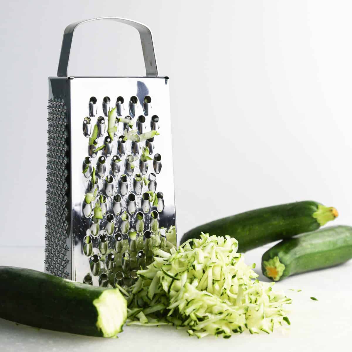 zucchini being shredded with a box grater to make zucchini cookies