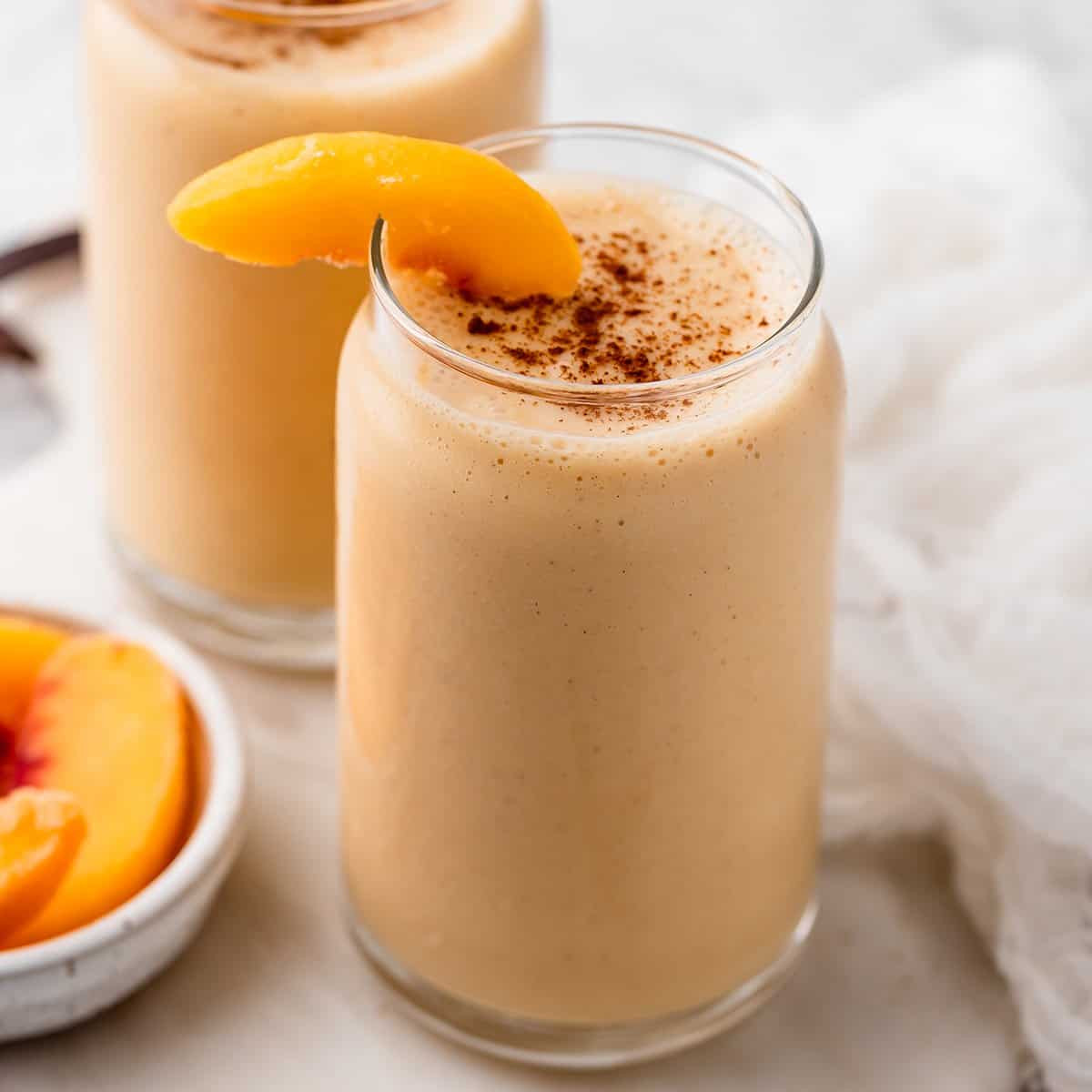 a glass of Peach Smoothie garnished with peach slices and sprinkled with cinnamon