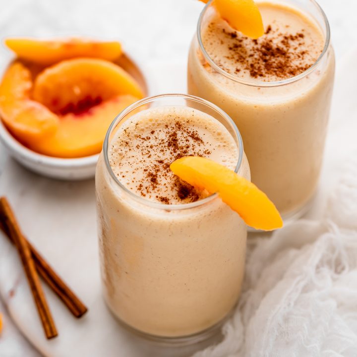 two glasses of Peach Smoothie garnished with peach slices and sprinkled with cinnamon